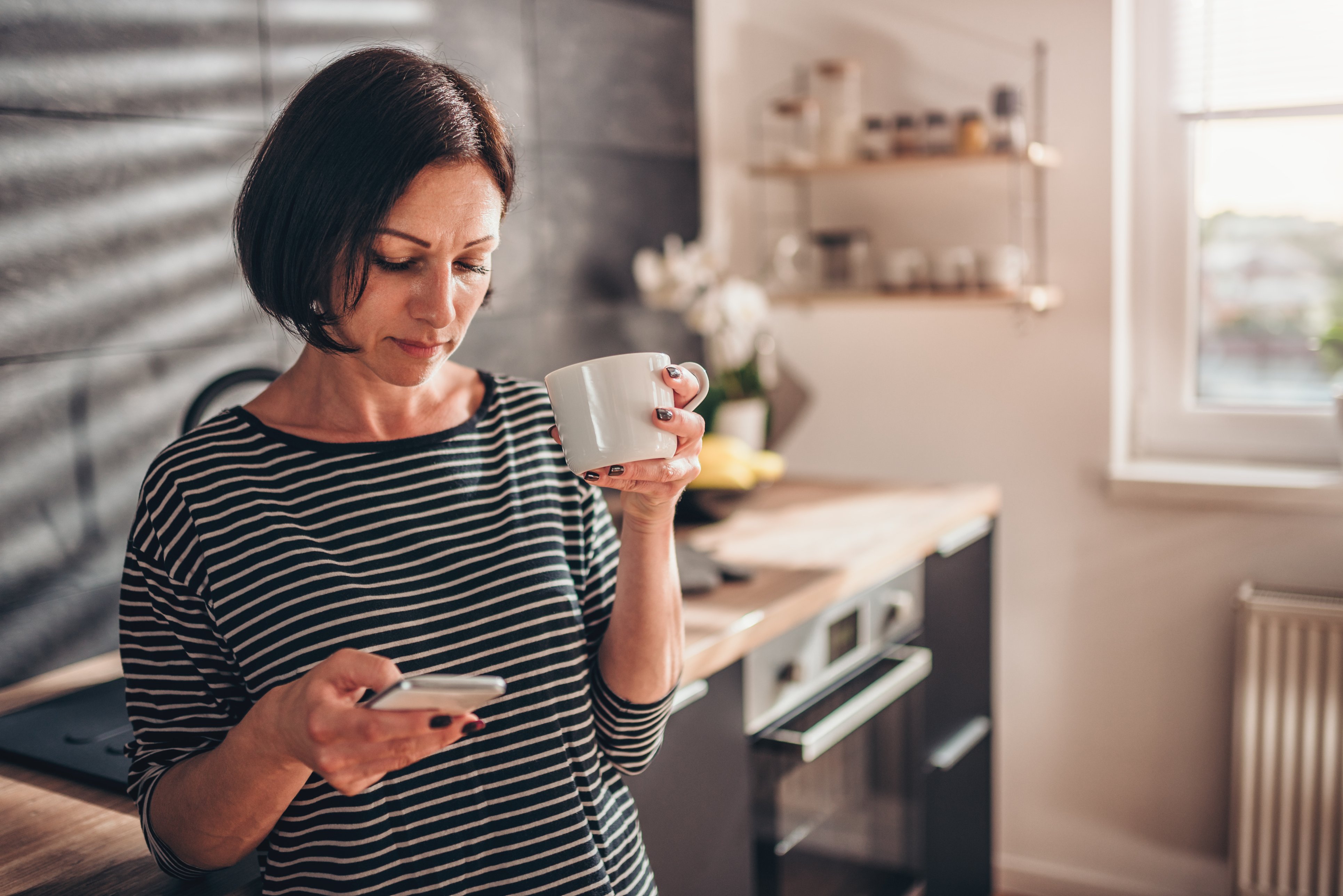 Woman standing in the kitchen and using smart phone